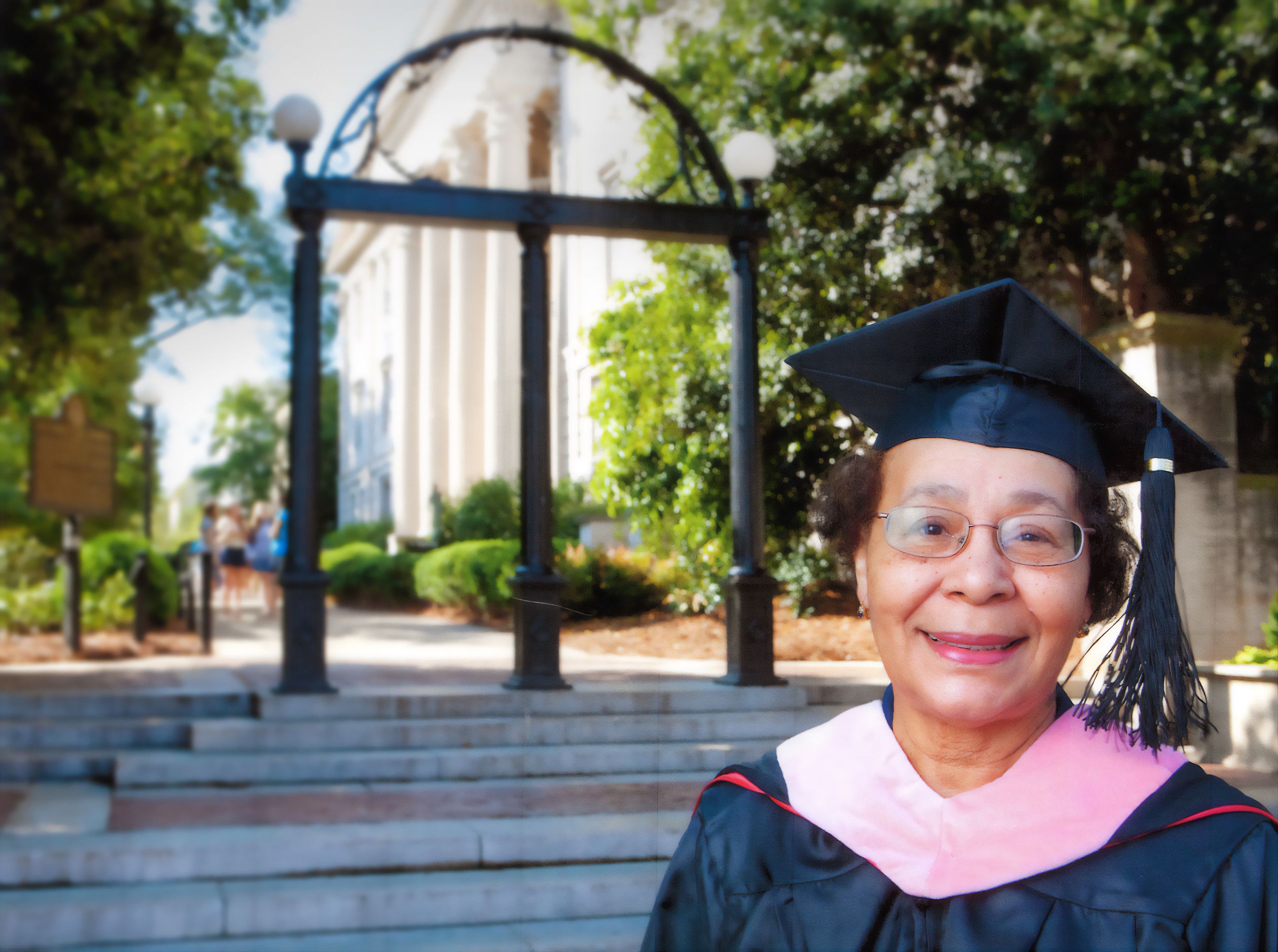 Mary Frances Early, wearing a cap and gown, poses for a photo in front of the Arch in 2012, on the 50th anniversary of her graduation from the university.